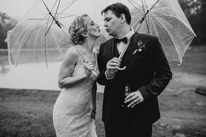 bride and groom pretending to kiss in the rain