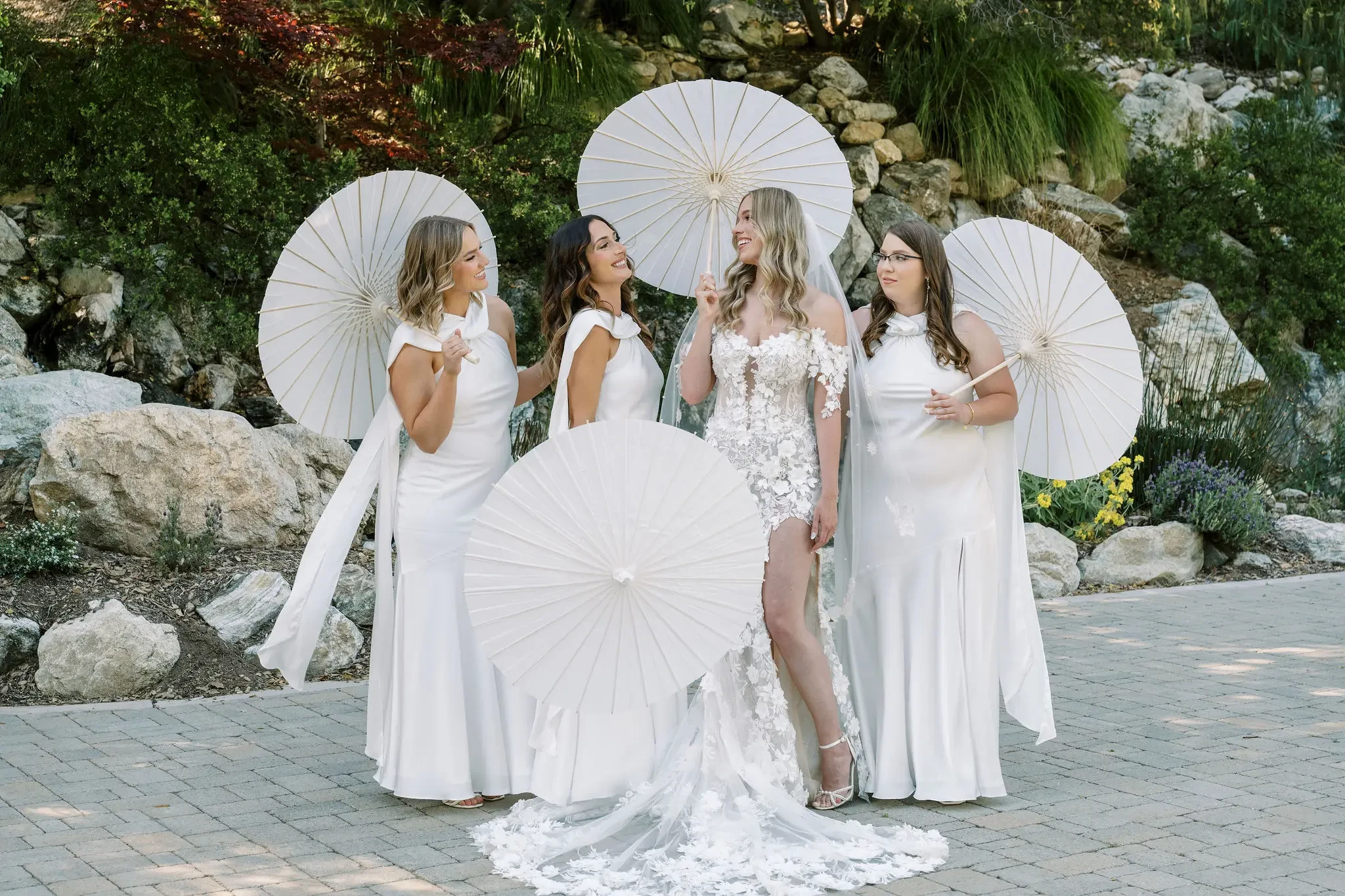 image shows bride with her bridal party holding white parasols 