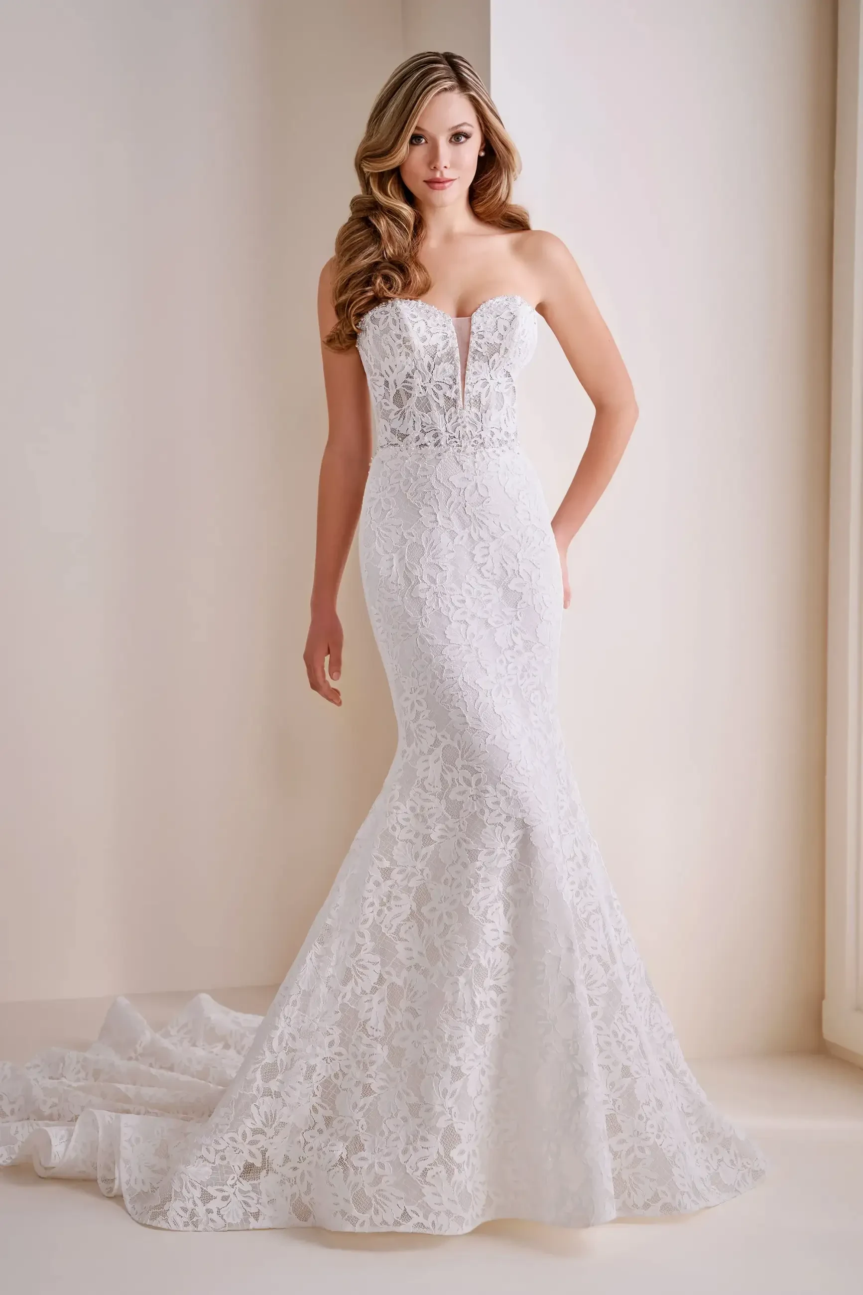 Model is wearing an allover lace mermaid wedding dress in ivory and nude with a plunging sweetheart neckline, dropped waist, and strapless fit.