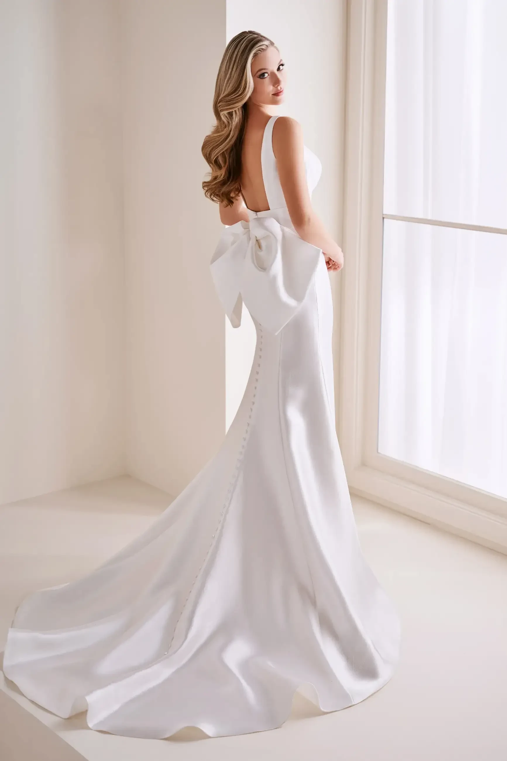 Model is wearing a sleek Mikado mermaid gown with a sweetheart neckline and a detachable oversized back bow.