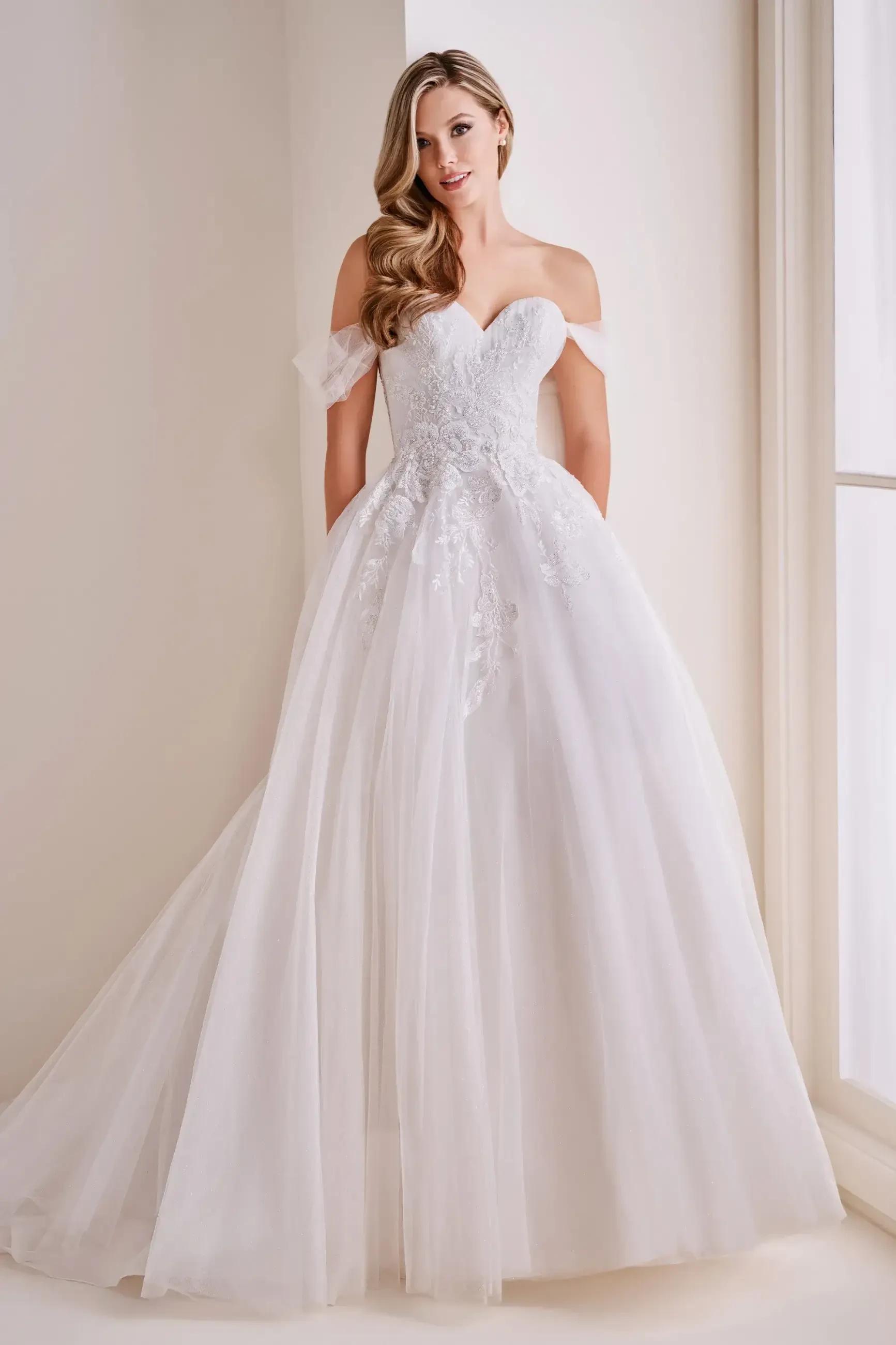 Model is wearing a glitter tulle ball gown with lace appliqués, a sweetheart neckline, lace-up corset back, and detachable lace straps.
