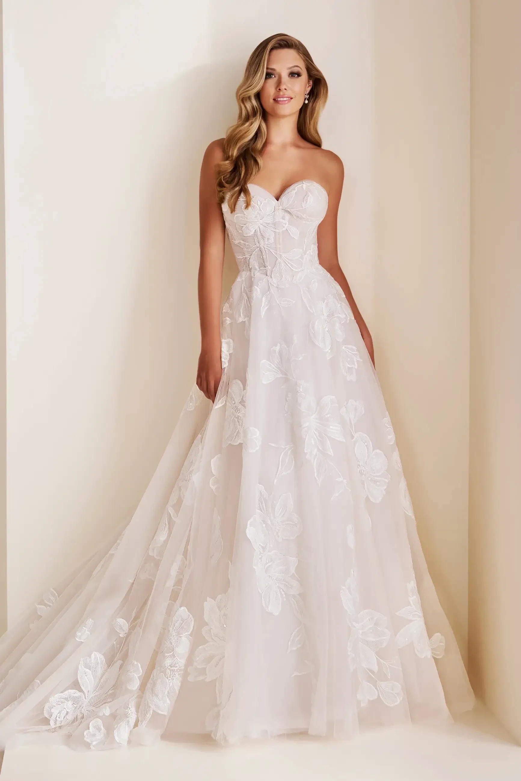 Model is wearing a romantic A-line gown with a sweetheart neckline, Schiffli lace appliqué, shimmering sequins, and layered tulle.