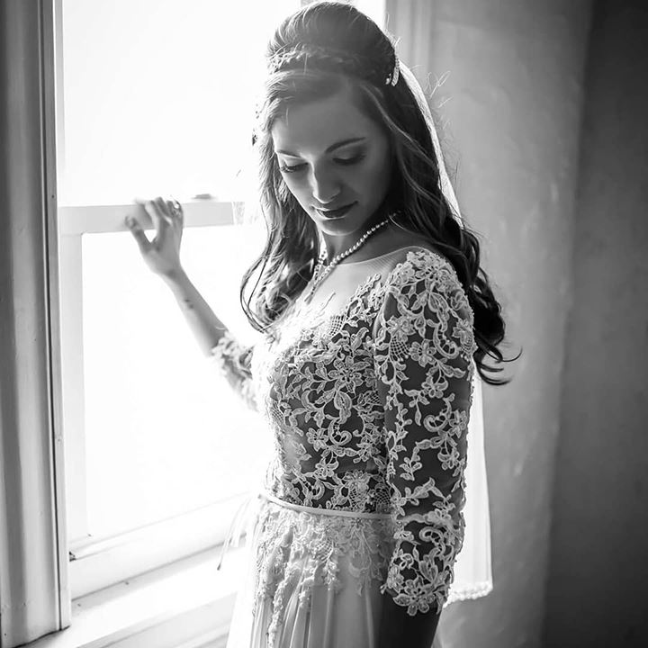 Bride wearing lace wedding dress and standing in front of window